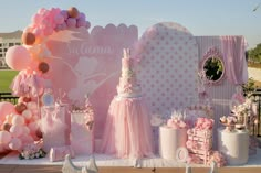 a pink and white dessert table with balloons, cake and other decorations on it's side