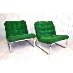 two green chairs sitting on top of a wooden floor next to each other in front of a white wall