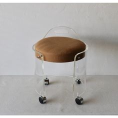 a clear chair with wheels and a brown seat cushion on the back is sitting in front of a white wall