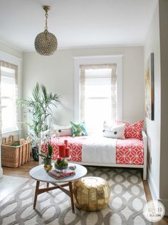 a living room with a bed, coffee table and rugs on the floor in front of two windows