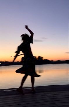 a woman is dancing on the dock at sunset