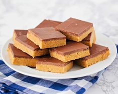 several pieces of chocolate peanut butter bars on a white plate next to a blue and white checkered napkin