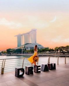 a woman standing in front of the word dream on top of a building next to water