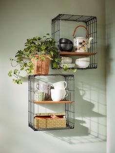 two metal shelves with plants and mugs on them in the corner of a room