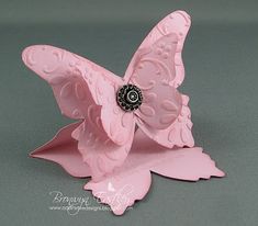 a pink butterfly figurine sitting on top of a gray surface with its wings open