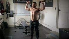 a shirtless man holding two dumbbells in a gym with his hands behind his head