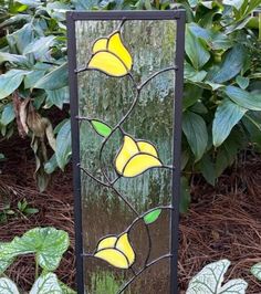 a stained glass panel with yellow flowers on it in front of some plants and leaves