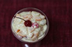 a dessert with cherries and nuts in a glass on a red tableclothed surface