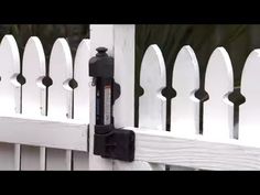 a white picket fence with a black light on the top and an iron gate handle