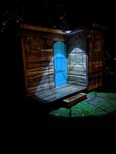 an outhouse in the dark with a blue door and window lit up at night