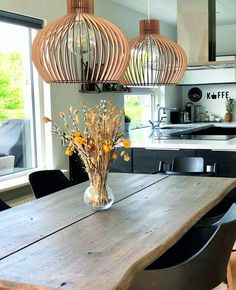 a wooden table topped with a vase filled with flowers next to two hanging lights above it