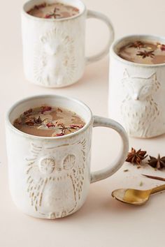 three white mugs filled with different types of tea and spices on top of a table