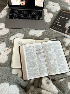 an open book sitting on top of a bed next to a laptop computer