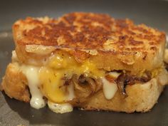 a grilled cheese sandwich with mushrooms and melted cheese on the top is sitting on a black plate