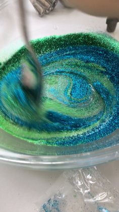 someone is painting something blue and green on a plate with glitter in the middle,