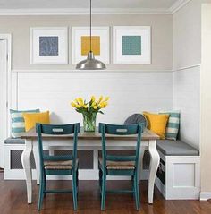 a dining room table with blue chairs and yellow flowers on the centerpiece, in front of white paneled walls