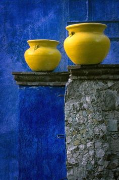 two yellow vases sitting on top of a stone pillar in front of a blue wall