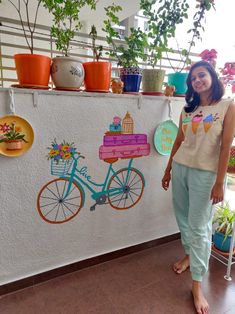 a woman standing in front of a wall with potted plants on top of it