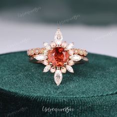 an orange and white diamond ring sitting on top of a green velvet box