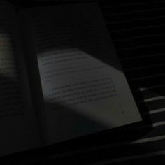 an open book sitting on top of a bed next to a window with the shadow of a person's hand