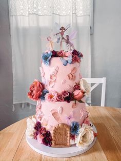 a three tiered pink cake decorated with flowers and fairy figurines