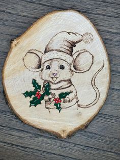 a wood slice with a drawing of a mouse wearing a santa hat and holly berries