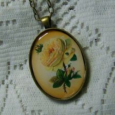 a necklace with flowers on it sitting on a lace tablecloth covered surface, next to a gold chain