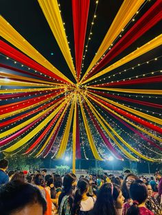 a large group of people standing in front of a tent with red, yellow and white streamers hanging from the ceiling