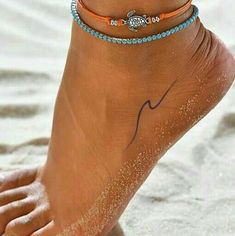 a woman's foot with two bracelets on it, and one ankle in the sand