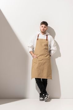 a man standing in front of a white wall with his hands on his hips wearing an apron