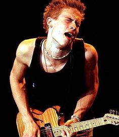 a young man playing an electric guitar in front of a microphone and wearing a black tank top