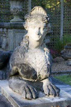 a statue of a woman sitting on top of a stone slab in a garden area