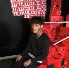 a man with tattoos sitting in front of some red speakers and looking at the camera