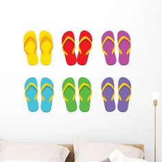 four pairs of colorful flip flops in front of a white wall with a bed