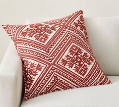 a red and white pillow sitting on top of a white couch next to a wall