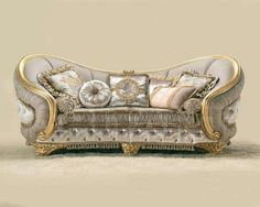 an ornate couch with gold trimmings and pillows on the back, in front of a beige wall