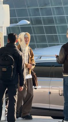 two men are standing in front of a car talking to each other while another man is on his cell phone