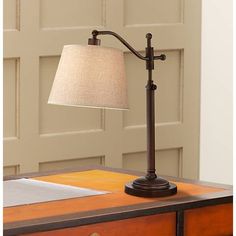 a lamp on top of a wooden desk next to a door with a white linen shade