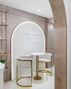 the magic is here sign on the wall behind two white chairs and a round table