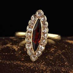 a gold ring with a large red stone surrounded by small white diamonds on top of a wooden surface