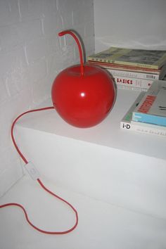 a red apple sitting on top of a white shelf next to books and a charger