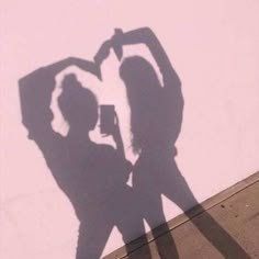 the shadow of two people standing next to each other in front of a pink wall