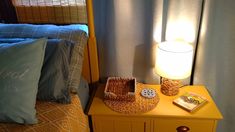 a yellow nightstand with a basket on it next to a bed