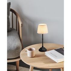 a table with a lamp, coffee cup and book on it next to a chair