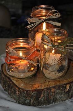 three mason jars filled with candles sitting on top of a piece of wood next to each other