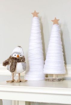 two small white christmas trees sitting on top of a table next to each other and one bird figurine