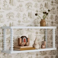 a shelf with some books and toys on it in front of a wallpapered background