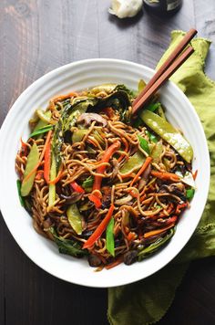 a white bowl filled with noodles and veggies on top of a wooden table