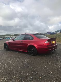 a red car parked in a parking lot with other cars behind it and cloudy skies above