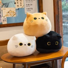 three stuffed cats sitting on top of each other in front of a wooden table next to a window